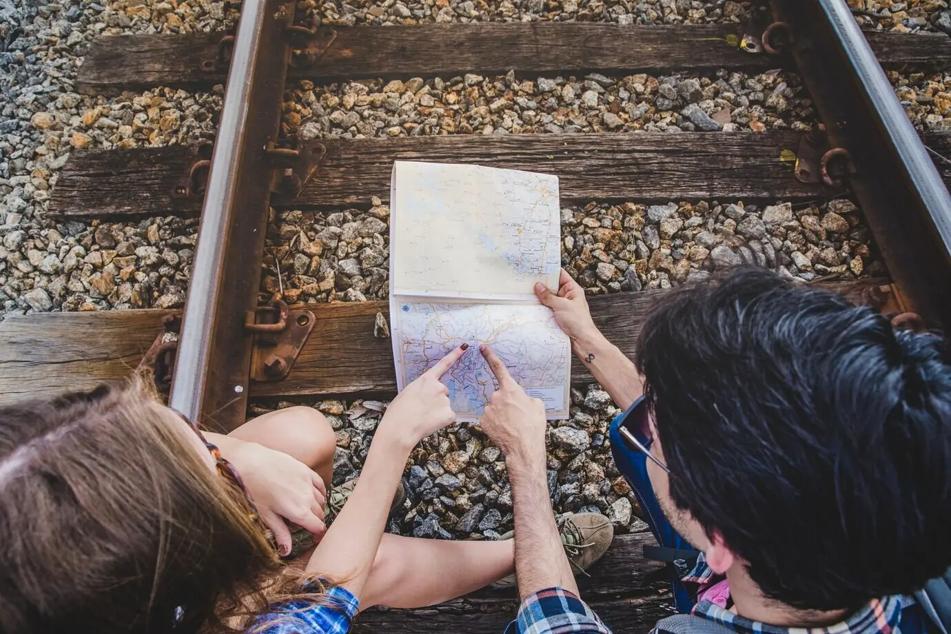 Junges Paar auf den Bahngleisen zeigt auf eine Karte.